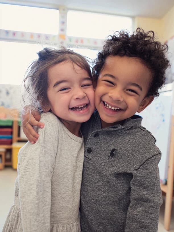 Zwei Kinder halten sich im Arm und lachen in die Kamera