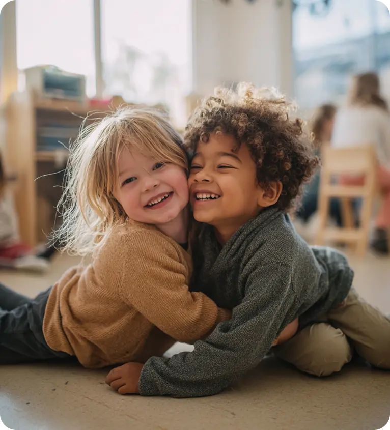 Zwei Kinder sitzen auf dem Boden und lachen in die Kamera